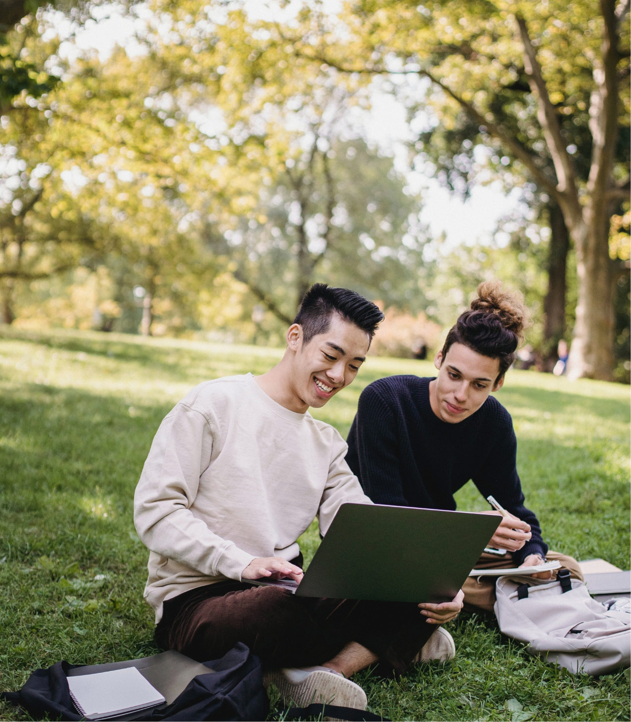 2 students sitting in a park working on a computer